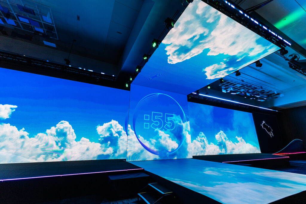 A brightly lit stage with large digital screens displays a vivid blue sky and white clouds, featuring a countdown timer reading 55 seconds at the center—a striking setting perfect for corporate videography in Boston.