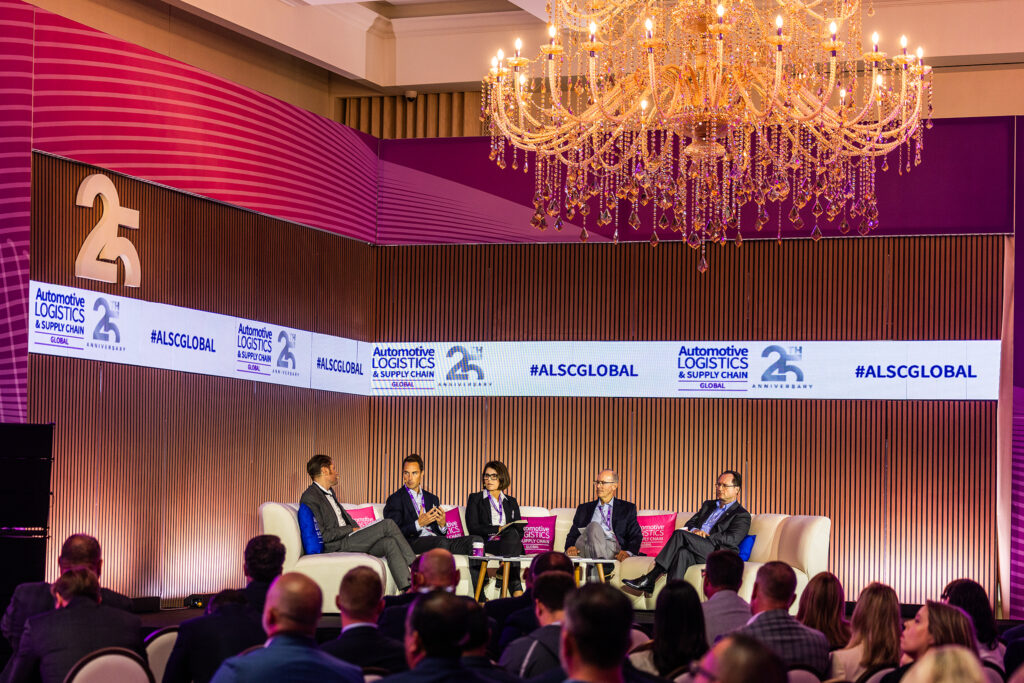 A panel of five people discusses onstage at the Automotive Logistics and Supply Chain Global conference at St Johns Resort, Detroit. A large chandelier hangs overhead, and the audience watches as event branding and #ALSCGLOBAL appear in the background.